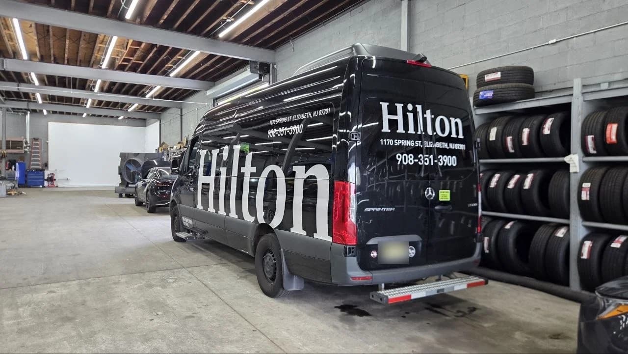 A Hilton-branded Mercedes-Benz Sprinter beside stocked tire racks in the Newark shop